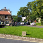 Picture of Osmotherley village green, showing the village cross and stone table (July 2021)